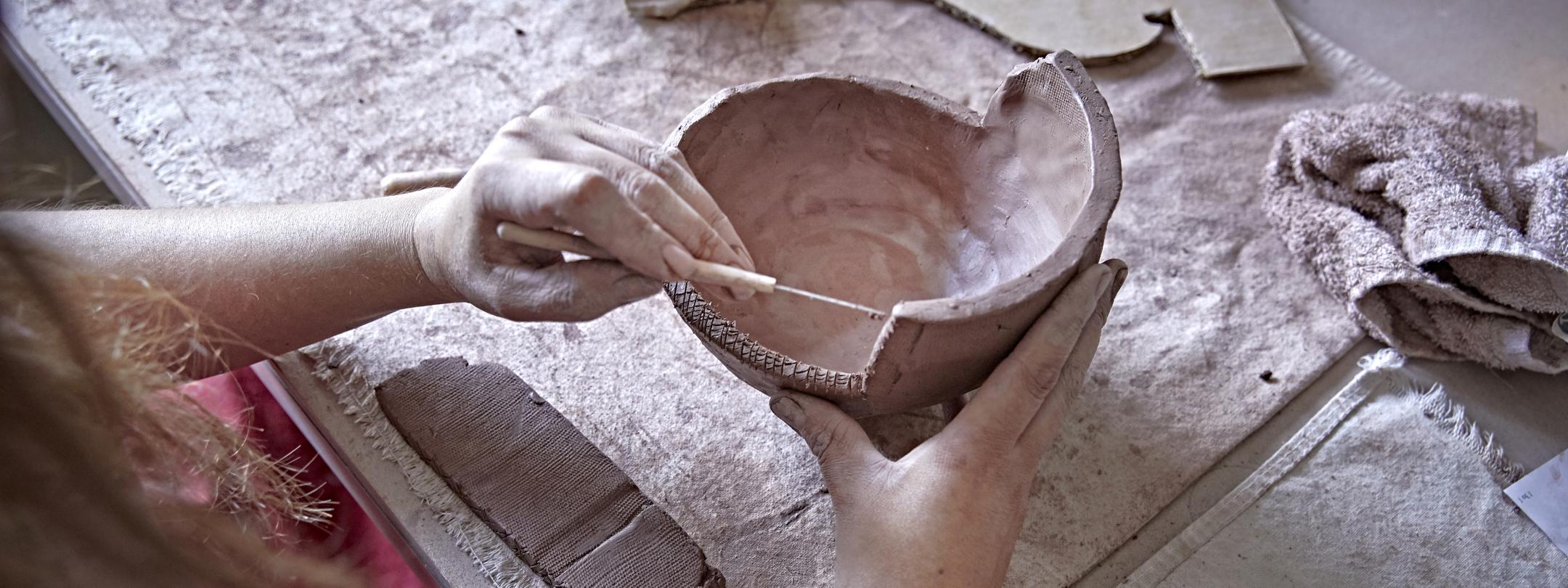 Close up of hands using a tool to work with a ceramics project